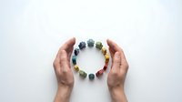 Hands protecting colorful gemstone circle arrangement on white background. Natural healing crystals and stones for wellness, meditation and energy work.