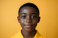 Young African American boy wearing yellow polo shirt smiling at camera against vibrant yellow background, expressing confidence and joy in studio portrait setting.