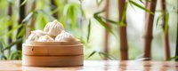 Steamed dumplings in traditional bamboo steamer on wooden table with green bamboo forest background, Asian cuisine setting in natural light.