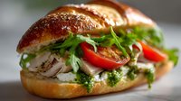 Gourmet sandwich with grilled meat, fresh arugula, red peppers and pesto sauce on artisan bread roll for restaurant menu and food advertising.