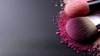 Professional makeup brushes with scattered pink and purple cosmetic powder on dark background for beauty industry advertising.