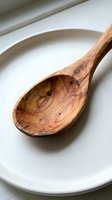 Handcrafted wooden spoon with natural grain patterns resting on ceramic plate, rustic kitchen utensil for cooking and serving organic food preparation.