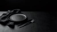 Empty plate with fork and knife on dark surface with fabric napkin, minimalist table setting for restaurant, dining, or food service design projects.