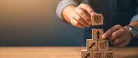 Businessman building wooden blocks with target icons in stair formation representing goal achievement and strategic planning for business growth and success.