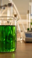 Glass beaker with bright green chemical solution in modern laboratory setting for scientific research and experimentation.