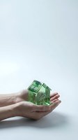 Hands holding transparent green glass house model symbolizing eco-friendly real estate, sustainable housing and environmental protection concepts.