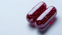 Red transparent capsules filled with small spherical supplements on light background, macro pharmaceutical shot for medical and healthcare marketing.