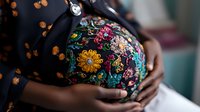 Pregnant African American woman's belly with colorful floral embroidered dress, hands gently cradling baby bump in soft natural lighting, capturing tender maternal moment.