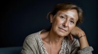 Thoughtful mature Caucasian woman in beige sweater resting chin on hand against dark background, expressing contemplation and wisdom in portrait style.