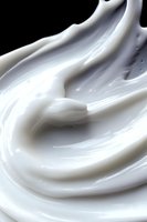 Smooth swirling white cream texture with glossy surface and soft curves creating elegant abstract pattern against dark background. For cosmetic and food industry.