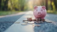 Pink piggy bank with scattered coins on asphalt road with blurred natural background representing savings, financial planning and money management concepts.