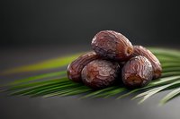 Fresh Medjool dates arranged on palm leaves against dark background for healthy snacking and Middle Eastern cuisine concepts.