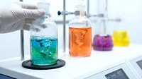 Laboratory scientist in white gloves conducting chemical experiment with colorful solutions in glass beakers on modern lab equipment for research analysis.