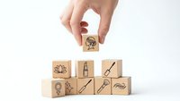 Hand placing wooden cube with brain icon onto pyramid of blocks featuring creative symbols for business strategy and innovation concepts.