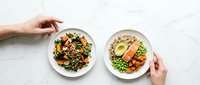 Fresh healthy meal bowls with grilled salmon, quinoa, roasted vegetables and greens on white marble background. Nutritious lunch or dinner concept.