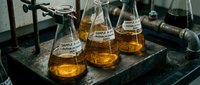 Chemical samples in laboratory flasks containing amber liquid on dark stone surface, scientific research and analysis setup for educational or industrial testing purposes.