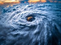 Dramatic aerial view of hurricane eye with swirling clouds illuminated by golden sunset light. Powerful weather system photographed from above showing nature's raw force.