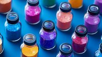 Vibrant glitter powder in glass jars with black lids arranged on blue background. Colorful craft supplies featuring pink, purple, blue and gold sparkles for decoration.