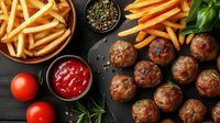 Delicious homemade meatballs with golden french fries, ketchup and spices on dark wooden background. Comfort food meal ready to serve.
