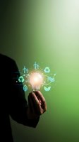 Businessman holding glowing light bulb with eco-friendly icons on green background representing sustainable energy innovation and environmental solutions.