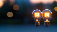 Two glowing vintage filament light bulbs against dark blurred background with bokeh lights creating atmospheric mood for creative and innovation concepts.