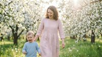 Happy mother and toddler son walking together in blooming spring orchard during golden hour sunset creating warm family bonding moment outdoors.