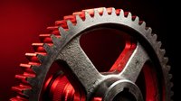Industrial metal gear wheel with teeth on red background for mechanical engineering and manufacturing concepts.