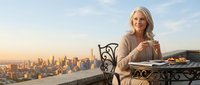 Mature blonde woman enjoying coffee on rooftop terrace overlooking city skyline at sunset, luxury lifestyle and urban living concept for wellness content.