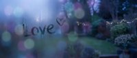 Love written on a foggy window with a heart, blurred garden lights in background, romantic rainy day mood in blue and purple tones.