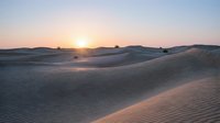 Serene desert landscape with rolling sand dunes at golden hour sunset, creating warm peaceful atmosphere for travel and nature concepts.