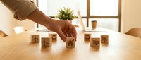 Hand arranging wooden blocks with business icons on desk representing strategy planning and organizational development in modern office.
