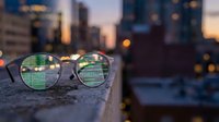 Eyeglasses on urban ledge with blurred city skyline at dusk, digital data reflection in lenses showing technology and vision concept for business analytics.