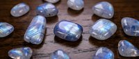 Polished moonstone gemstones with blue flash adularescence scattered on rustic wooden surface for jewelry making and crystal healing practices.