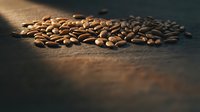 Roasted coffee beans scattered on rustic wooden surface with warm lighting creating aromatic cafe atmosphere for beverage and food industry concepts.