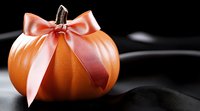 Orange pumpkin with elegant pink satin bow on black background, creating festive autumn decor for Halloween or Thanksgiving celebrations.