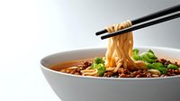 Steaming bowl of Asian noodle soup with chopsticks lifting ramen, garnished with green onions and spicy chili oil in white ceramic bowl on light background.