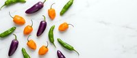 Colorful hot chili peppers in green, orange and purple varieties scattered on white marble background with copy space for culinary and cooking designs.