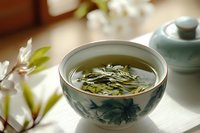 Traditional Chinese tea ceremony with green tea leaves steeping in porcelain bowl decorated with blue floral pattern, cherry blossoms in background, soft natural lighting.