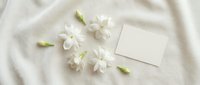 White jasmine flowers with buds arranged on neutral linen fabric alongside blank card for wedding invitations, greeting cards, and spring event designs.