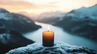 Glowing candle on snowy mountain peak overlooking serene lake and mountains at sunset, creating atmospheric winter meditation scene.