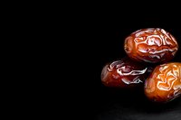 Fresh sweet dates on black background, close-up view showing natural texture and glossy surface of dried fruit. Middle Eastern delicacy with copy space.