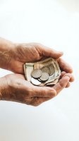Mature adult hands holding folded banknotes and coins against white background. Isolated stock photo suitable for financial, charity, savings, and business concepts.