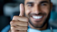 Young Hispanic businessman giving thumbs up gesture with confident smile in modern office environment for success and approval concepts.