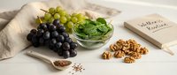 Fresh grapes, leafy greens, walnuts and seeds arranged on neutral linen background for healthy eating and nutrition concepts.