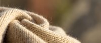 Closeup of soft beige knitted fabric texture with natural folds and wrinkles, suitable for fashion, textile, and apparel design projects.