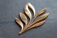 Elegant golden leaf brooch on dark textured background showcases delicate metalwork with flowing curves and organic design, highlighting jewelry craftsmanship and nature-inspired art.