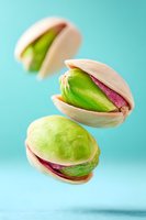 Fresh pistachio nuts floating in air against turquoise background, showing vibrant green kernels inside cracked shells in macro photography composition.