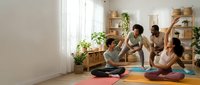 Diverse group of women practicing yoga together in bright, plant-filled studio space with wooden shelving and colorful mats during wellness class session.