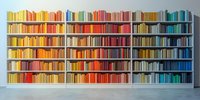 Books arranged by color spectrum on white library shelves creating rainbow pattern from yellow through red to blue. Modern minimalist interior design element.