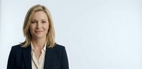 Professional blonde businesswoman in dark suit jacket smiling confidently against white background for corporate marketing materials.